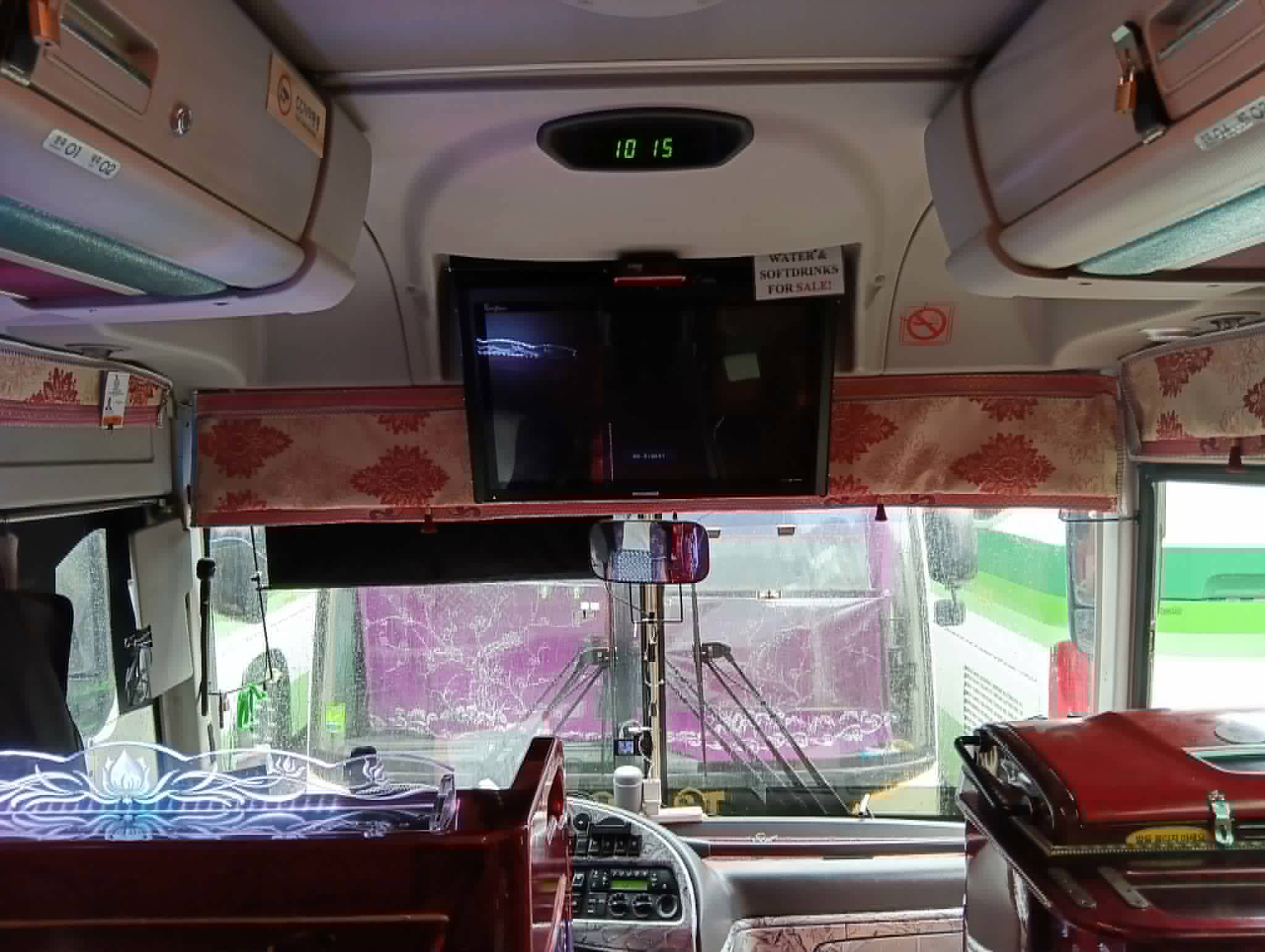 Overhead TV and digital clock above the driver's windscreen, with the no-smoking sign and drinks notice beside them.