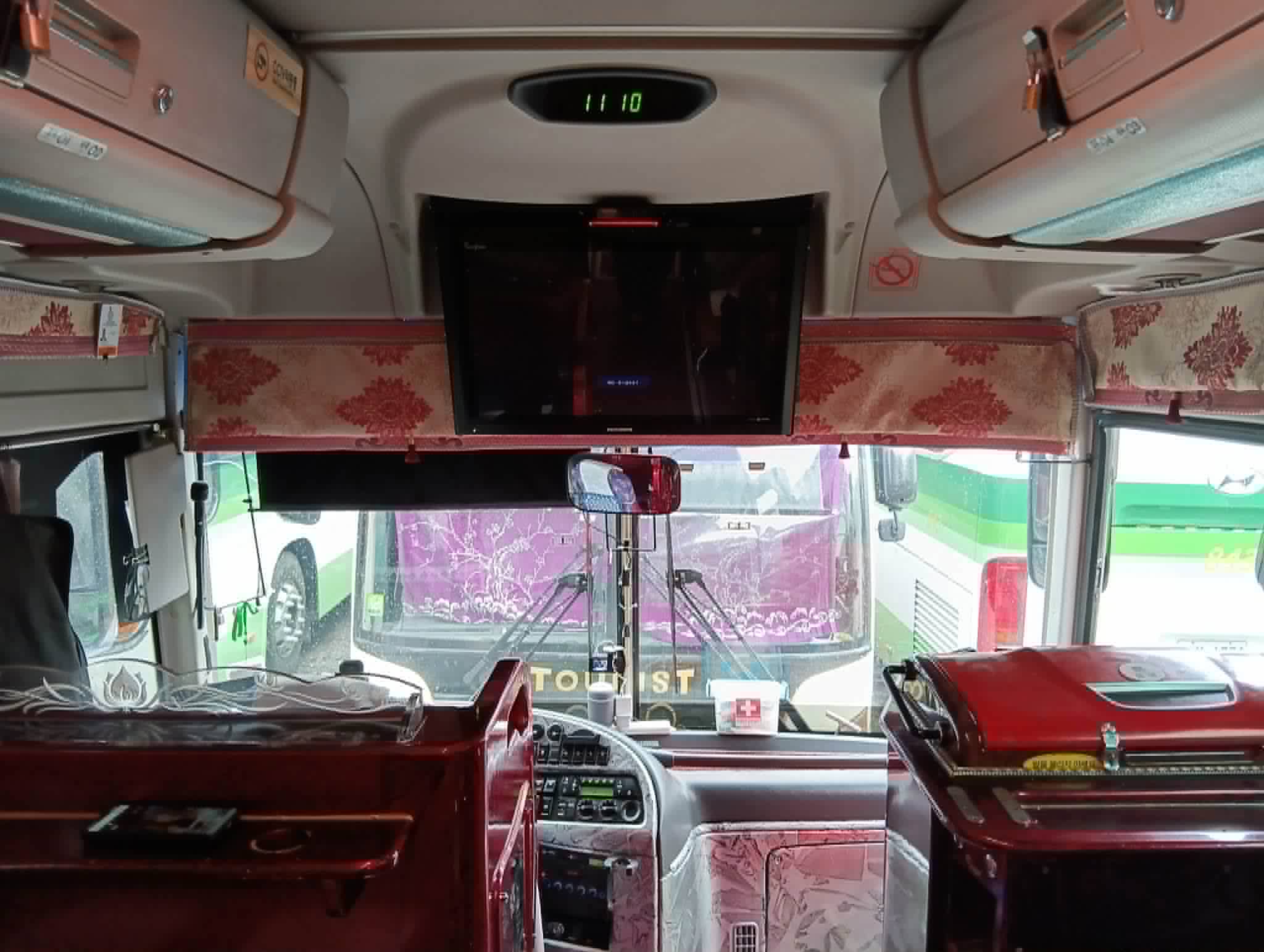 Driver's cockpit with the overhead TV folded down, curtained windscreen valance, and the dashboard below.