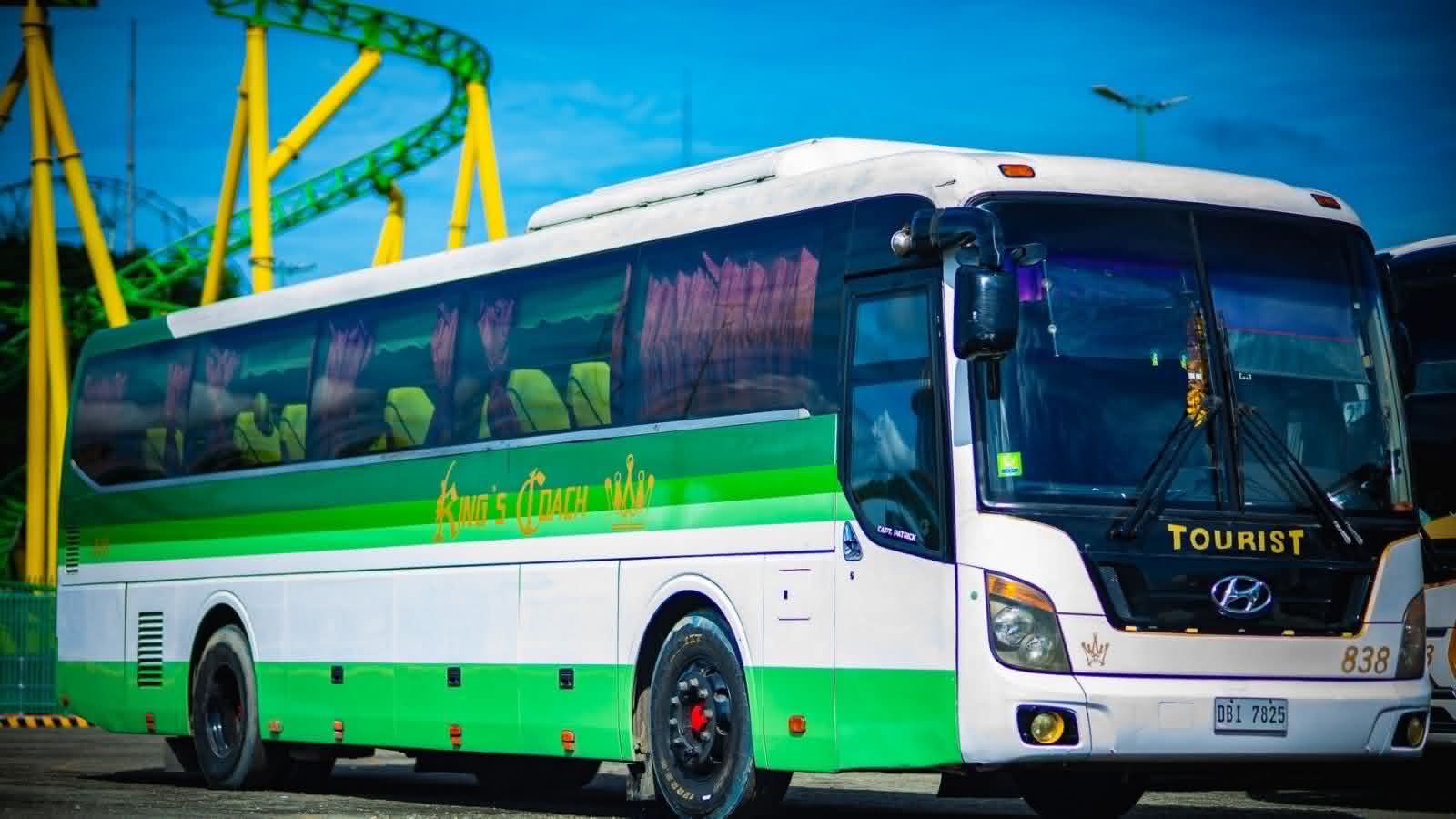 King's Coach tourist coach in green and white livery, parked at Enchanted Kingdom with the roller coaster in the background.